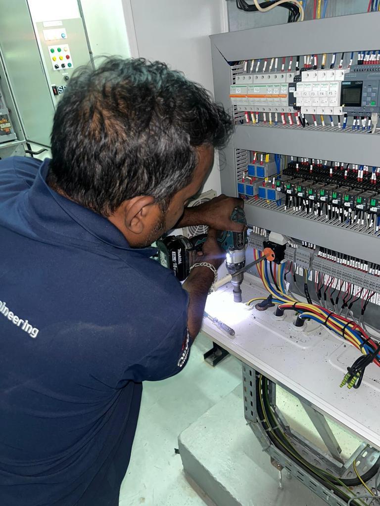 A technician wires breakers around a Siemens LOGO controller inside a live control panel.